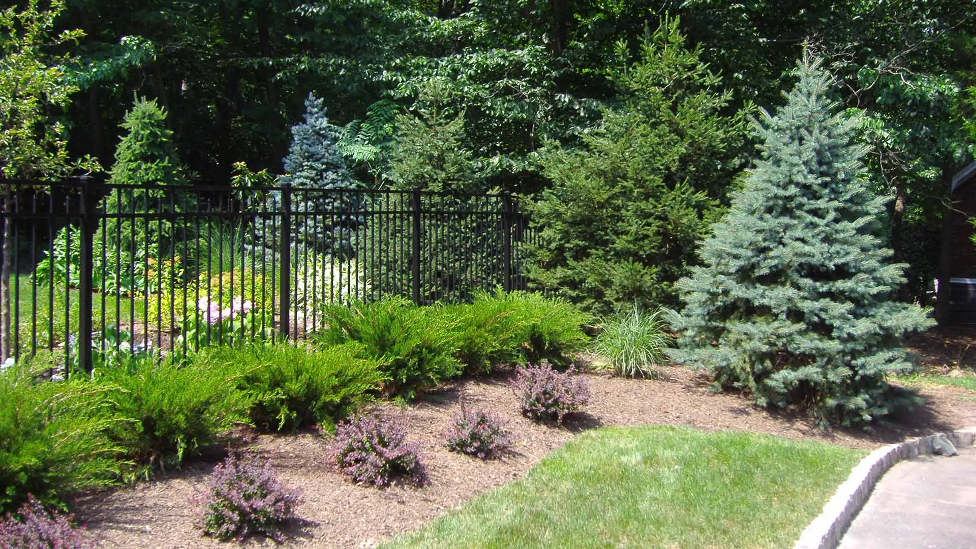 Beautiful plant bed around an iron fence on a home property in Warren, NJ.