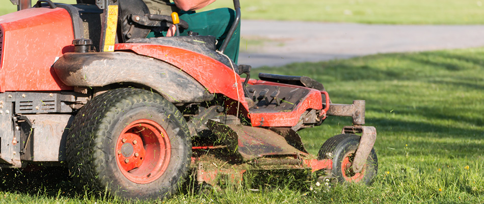 Lawn maintenance worker using a red riding mower to cut a lawn in Bridgewater, NJ